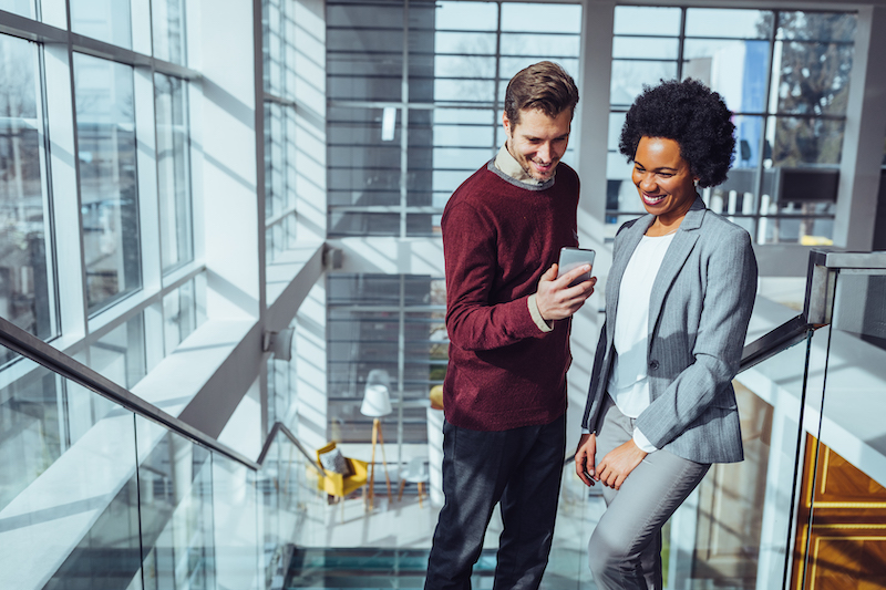 Business people in a corporate building smiling while looking at a smart phone