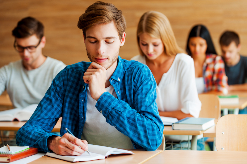 Focused on sat exam. Group of concentrated young students writing something in their note pads while sitting at their desks in the classroom