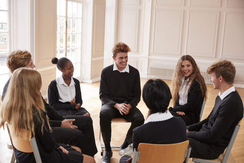 Group of high school students in debate club sitting in a circle talking and smiling