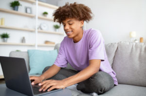 High school student sitting on the couch with a laptop writing a research paper