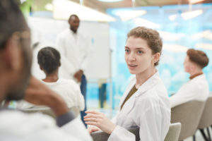 Portrait of young woman wearing lab coat while talking to man in medical school
