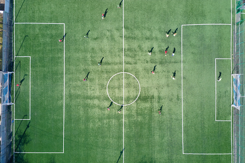 Aerial view of soccer players playing football on green sports stadium.