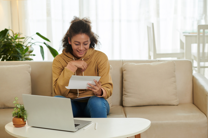 Girl smiling and sitting on the couch while opening acceptance letter from a university