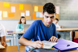 High school young student writing on notebook in class - Teenage boy sitting at desk doing exercise in classroom