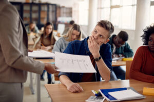 Displeased male student receiving bad test results from his professor at lecture hall.