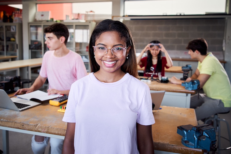 Portrait of a girl standing in a technology class looking at the camera. Vocational training students in classroom studying electronics, robotics, electricity of technical college.