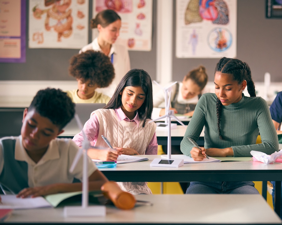 Secondary Or High School Students Studying Wind Turbines In Science Class With Teacher In Background