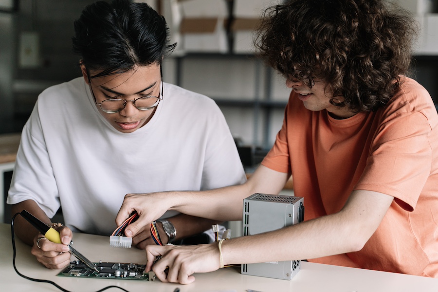 Two Friends Secondary School Students soldering together electronics circuit board device in the science technology workshop - Digital Innovation in Education