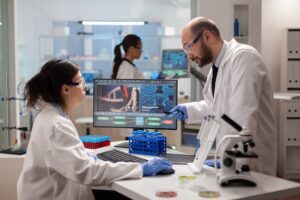 Scientist woring together to find a vaccine in healthcare lab looking at dna sample on computer. Chemists stuff analysing virus evolution using high tech technology for treatment research.