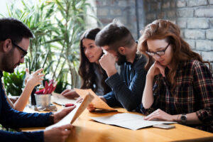 Graduate students preparing for the GRE exam together, reviewing study materials and practice tests in a collaborative setting