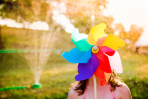 Beautiful girl in swimsuit hiding behind colorful pinwheel, sunny summer garden