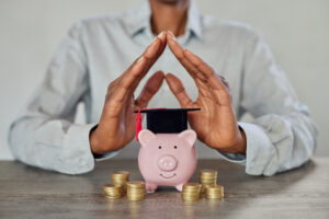 Close up of businesswoman hands showing sign of protection for graduation savings on piggy bank. Student loan, education savings and scholarship concept.