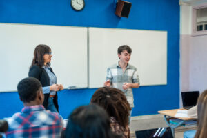 High school student giving presentation in classroom with teacher and students watching