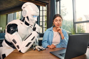 Young woman and a humanoid robot working while sitting at a laptop in a modern office. Collaboration between humans and artificial intelligence.