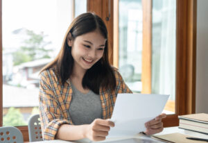 Young woman student is smiling and reading the good news in paper the letter while sitting to reading textbook in college.