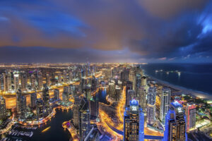 Cityscape of the Dubai, United Arab Emirates at dusk, with illuminated skyscrapers and coastline of the Persian Gulf.