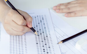 Students hand holding pencil writing selected choice on answer sheets and Mathematics question sheets. students testing doing examination. school exam